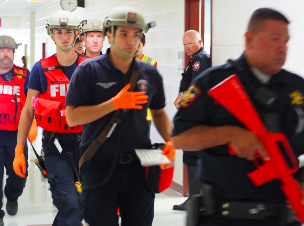 A security force escorts the second group of North Hays Fire/Rescue and EMS (medical support) personnel into the building. Multiple secured areas are set up by deputies for use by medical personnel to treat, stabilize, and prepare evacuation of the wounded.